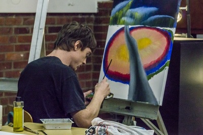 Man facing a canvas, mixing paint on a palette.