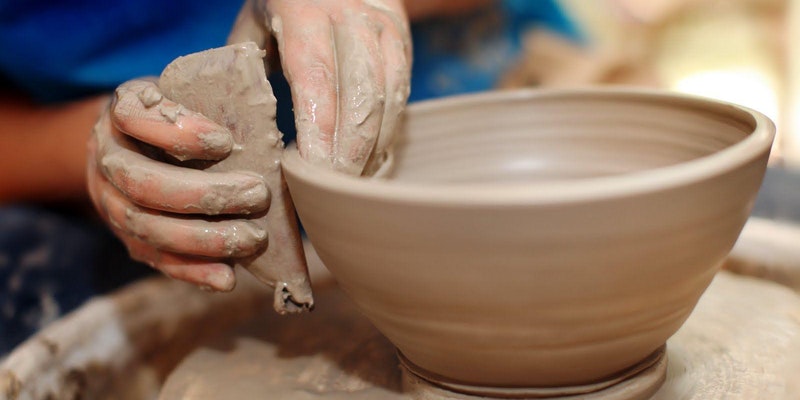 Hands pulling the edge of a clay bowl on a wheel.