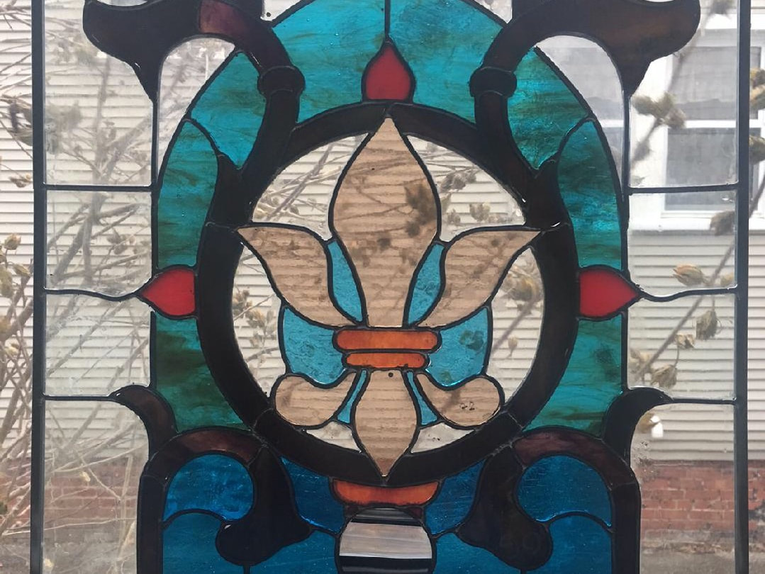 Stained glass window in clear, red, and blues with a fleur de lis.