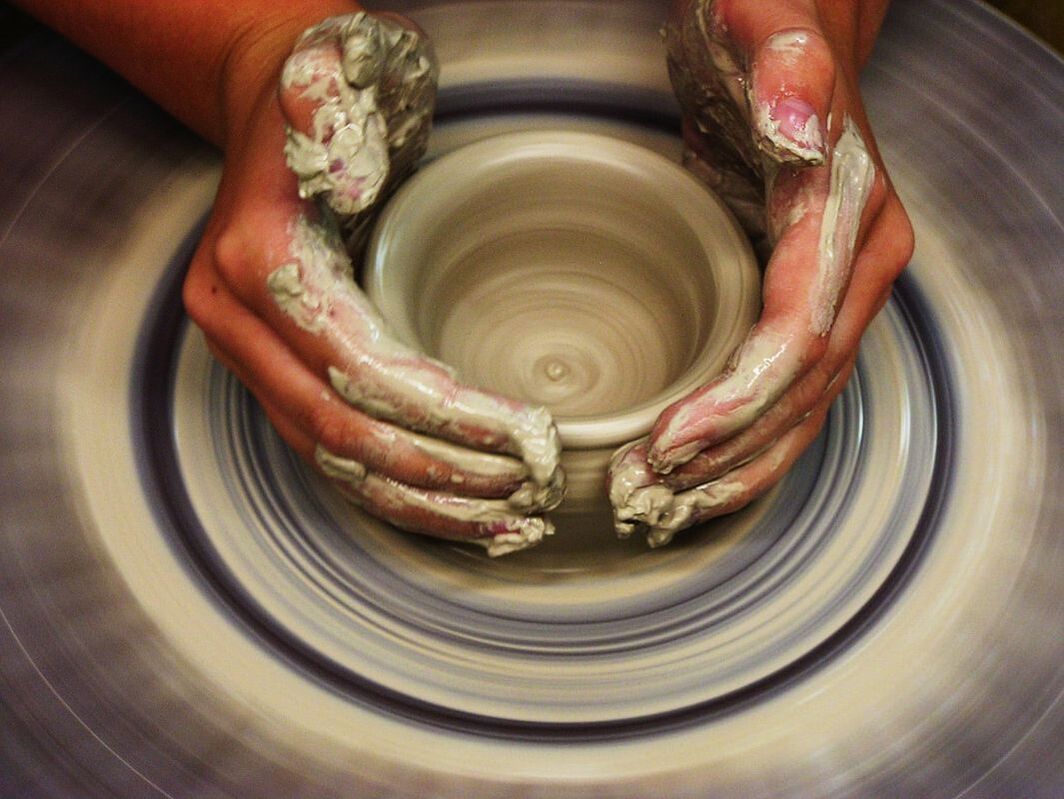 Two hands shaping a clay bowl on a ceramics wheeel.